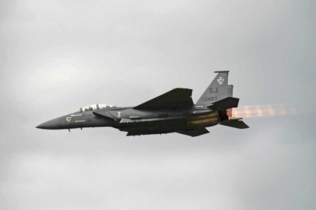 Dramatic view of F-15 fighter jet flying outdoors, showcasing afterburners against a cloudy sky.