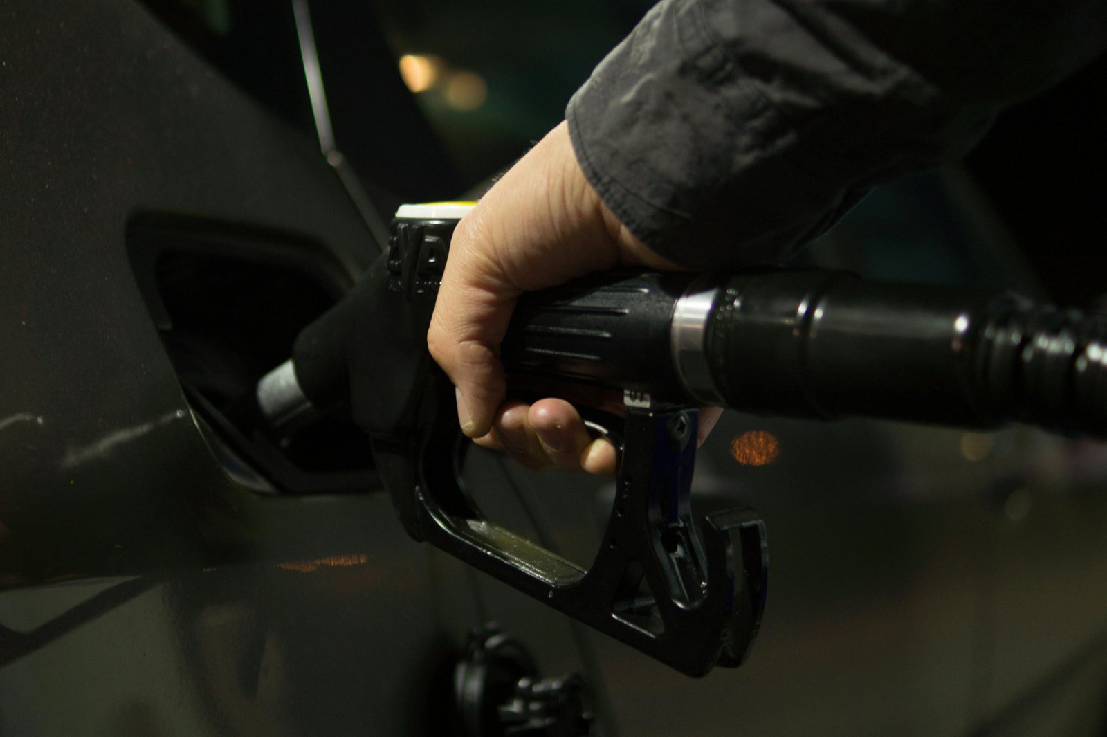 Close-up of a person refueling a car at a gas pump during night.